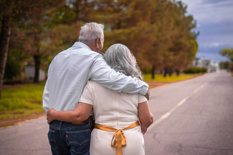 An older man and woman with grey hair walking arm in arm down a road